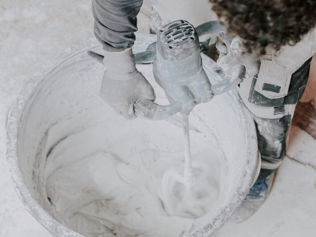 Un jeune homme caucasien, plâtrier, tient un mélangeur électrique de construction et remue du mastic sec avec de l'eau.