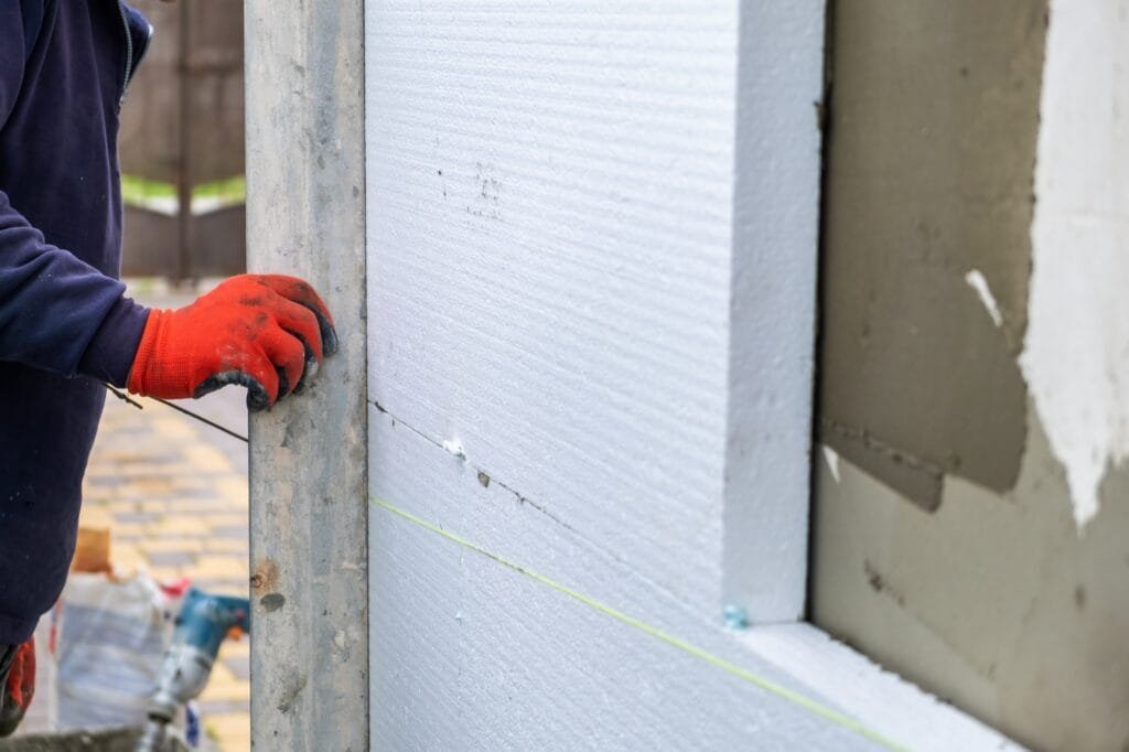 Trabajador de la construcción instalando planchas aislantes de espuma de poliestireno en la pared de la fachada de una casa