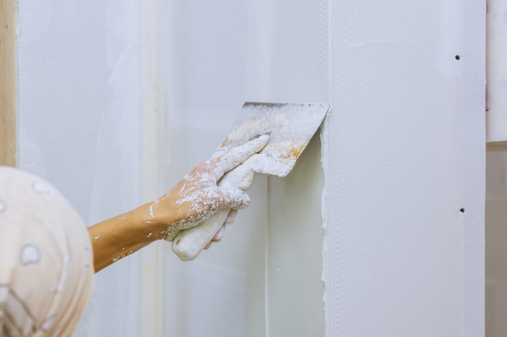 Homem repara uma parede com uma espátula de gesso numa parede