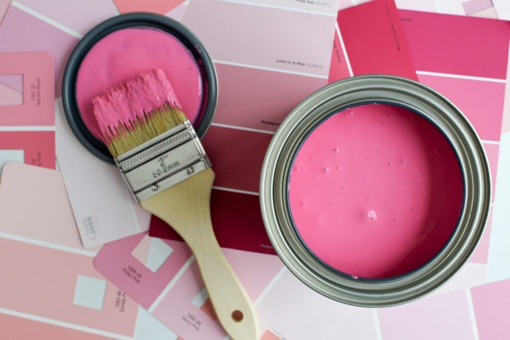 Bidon de peinture rose ouvert avec un pinceau et des échantillons de peinture rose