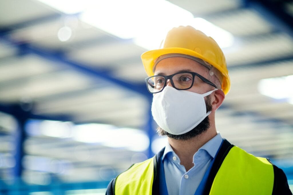 Technicien ou ingénieur avec masque de protection et casque debout dans une usine industrielle