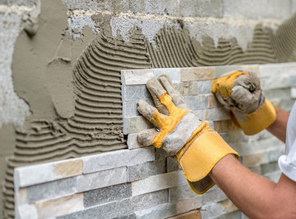 Muž vtlačující okrasnou dlaždici do lepidla na stěně