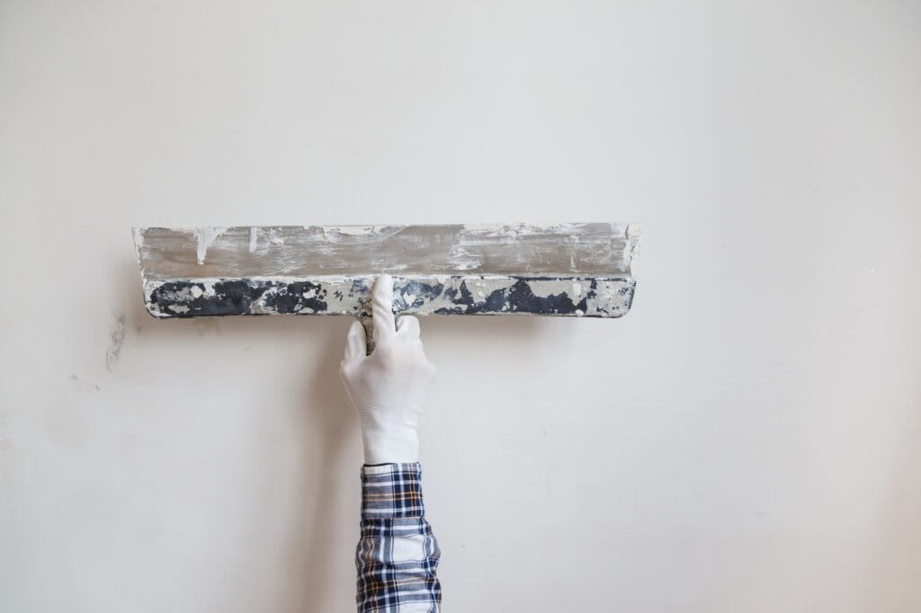 Un trabajador con guantes blancos realiza el enlucido de las paredes de la habitación.