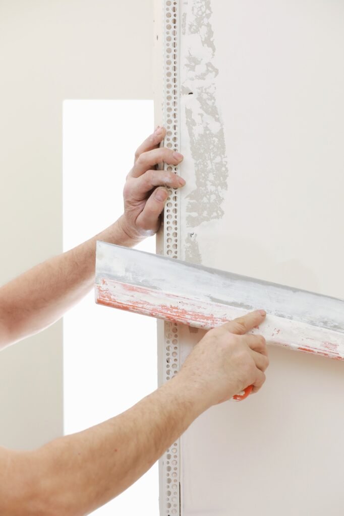 Bâtisseur portant un masque de protection et utilisant une truelle pour ajouter de l'enduit. Plâtrage d'un mur à l'aide d'un couteau à mastic.